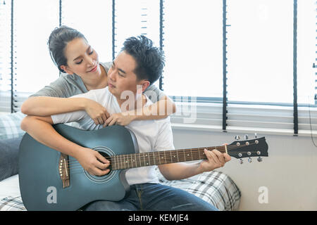 Coppie giovani suonare la chitarra tohether nella camera da letto di casa contemporanea per lo stile di vita moderno concetto Foto Stock