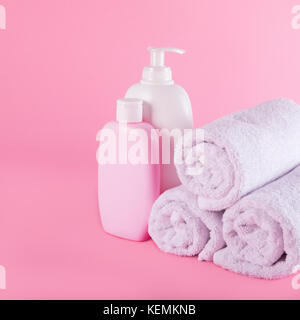 Asciugamani con il gel doccia e la lozione per il corpo su sfondo rosa Foto Stock