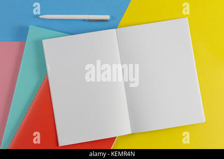 Aprire il notebook, penna bianca e colorate notebook su blu e sfondo giallo Foto Stock