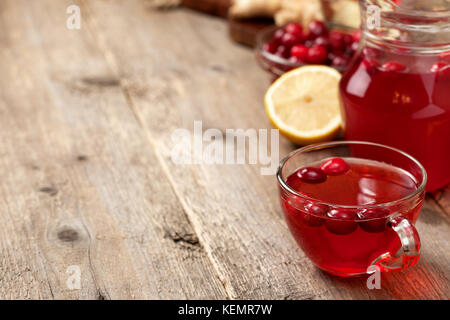 Mirtilli rossi con limone e zenzero drink in un bicchiere di vetro, miele, mezzo limone, fette di zenzero sul vecchio sfondo di legno Foto Stock