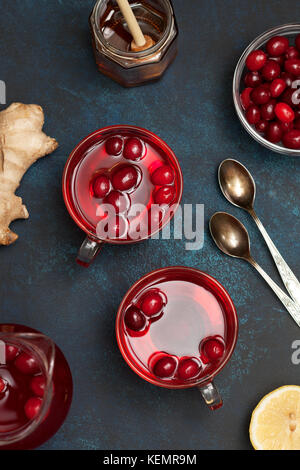 Mirtilli rossi con limone e zenzero drink in un bicchiere di vetro, miele, mezzo limone, fette di zenzero su uno sfondo blu Foto Stock