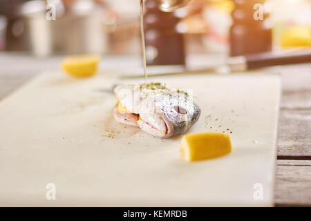 Versando con olio di pesce crudo. Il processo di cottura del pesce dorado close up. Il ristorante di pesce e di prodotti del mare. Foto Stock