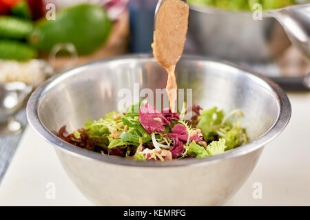 Versare la salsa in un recipiente con insalata mista. verde insalata sana in acciaio inox con una ciotola in ristorante. chef piatto di cottura sul lavoro. Foto Stock