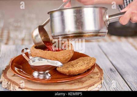 Lo chef versando borshch ucraine nel recipiente del pane. chef mettendo dalla pentola zuppa rossa in pentola dal pane tradizionale cibo ucraino. Foto Stock