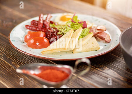 Prima colazione inglese sulla piastra. prima colazione inglese con toast, pomodori, fagioli, uova fritte, salsicce al forno e bakon. prima colazione inglese nel ristorante. Foto Stock