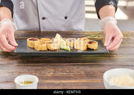 Lo chef mani tenendo la piastra con sushi rotoli. unagi sushi rotoli sulla tradizionale piatto giapponese in cook mani. sushi con anguilla e avocado. Foto Stock