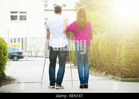 Vista posteriore della donna con il suo marito disabili permanente sulla strada Foto Stock