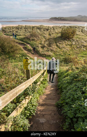 Segno di avvertimento di fasi irregolari e di un uomo che cammina verso il basso attraverso le dune a Alnmouth, Northumberland, Regno Unito con spazio di copia Foto Stock
