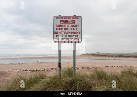 Segno di avvertimento non sicuri condizioni di balneazione nel fiume Tagliamento a Alnmouth, Northumberland, Regno Unito con la foce e la spiaggia in background con spazio di copia Foto Stock
