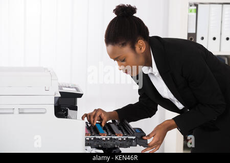 Giovane imprenditrice che fissa macchina fotocopiatrice in ufficio Foto Stock