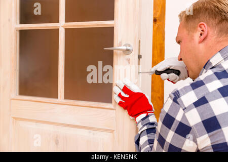 Tuttofare che fissa la porta con un cacciavite Foto Stock