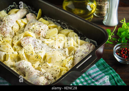 Materie le cosce di pollo con patate crudo nella maionese in forma per la cottura su un tavolo di legno. degli ingredienti a base di carne per cucinare. ricetta. Foto Stock