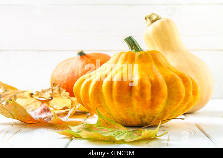 Zucca e Patty pan e acero, rovere foglie gialle su una bianca tavolo in legno. raccolto autunnale. Foto Stock