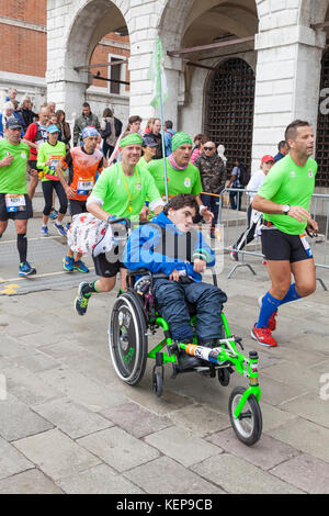 Venezia, Veneto, Italia Il 22 ottobre 2017. I partecipanti e guide in Venice Marathon avvicina il traguardo passando per San Marco sul ponte della Paglia. In primo piano è un gruppo da qual buon vento spingendo un giovane ragazzo di disabili in sedia a rotelle di nome Riccardo. Foto Stock