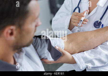 Medico dà una iniezione intramuscolare in braccio maschio Foto Stock
