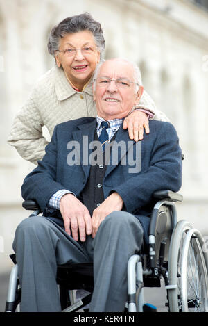 Senior uomo essendo spinto dalla moglie in carrozzella Foto Stock