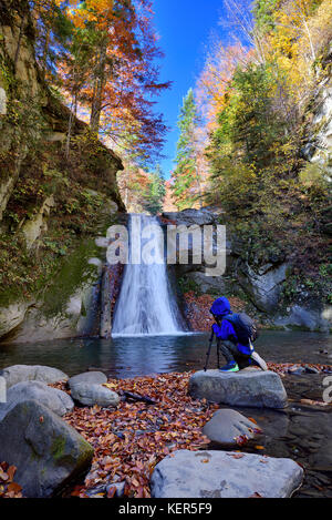 Capretto felice vicino a foto fotocamera sul cavalletto con una cascata in background in autunno Foto Stock