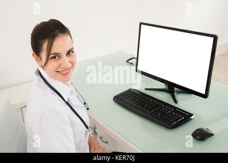 Felice medico donna seduta nella parte anteriore del computer in clinica Foto Stock