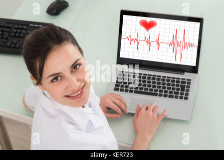 Felice femmina giovane medico con laptop mostra heartbeat Foto Stock
