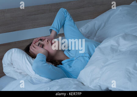 Giovane donna che soffre di cefalea giacente sul letto Foto Stock