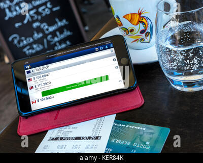 Moneta di Scambio app sulla schermata di iPhone nel ristorante francese di pagamento di bollette situazione all'estero, la carta Amex & euro bill sul tavolo. (Carta alterata in modo sicuro) Foto Stock