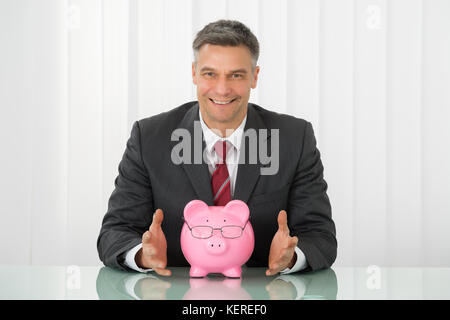 Happy businessman con piggybank indossando occhiali sulla scrivania Foto Stock