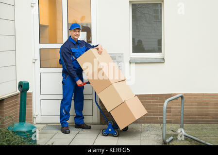 Felice coppia consegna uomo scatole di contenimento su un carrello Foto Stock