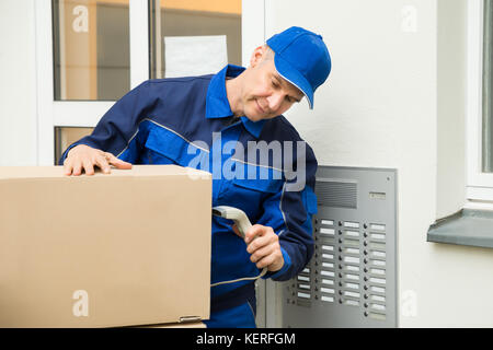 Maturo uomo consegna la scansione di scatole di cartone con uno scanner di codici a barre Foto Stock