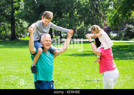 La famiglia felice divertirsi facendo Piggyback Ride con i bambini nel Parco Foto Stock