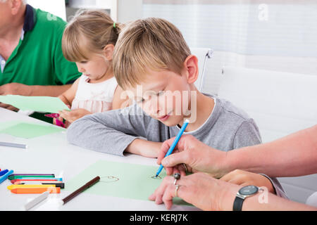 Nonni aiutando i loro nipoti per disegnare su carta colorata in casa Foto Stock