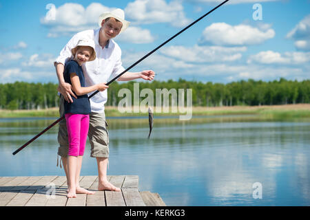 Papà aiuta la figlia per la cattura di pesce con una canna da pesca sul fiume Foto Stock