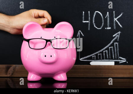 Persona mettendo mano una moneta nel salvadanaio di fronte blackboard mostra grafico Foto Stock