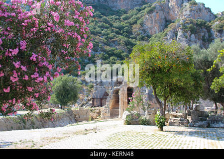 Pittoresche vedute delle rovine del teatro antico sullo sfondo di montagne, alberi fioriti con fiori viola e frutta di arance in Myra Foto Stock