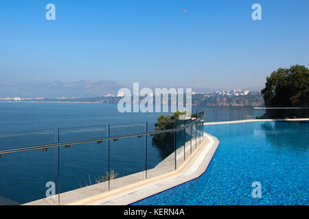 Una vista della piscina e del mare turchese con acqua chiara con una gamma di montagna all'orizzonte e la linea della costa mediterranea con il resort Foto Stock