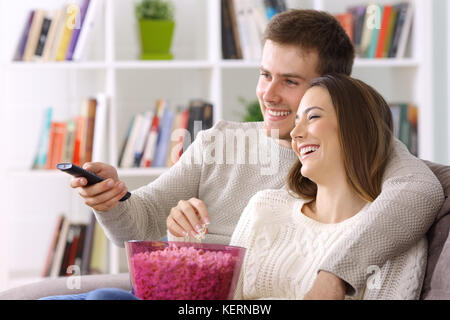 Coppia felice guardando la TV seduti su un lettino a casa in inverno Foto Stock