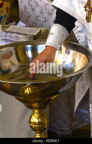 Close up font con acqua per il battesimo con il sacerdote e il rostro in background in chiesa ortodossa Foto Stock