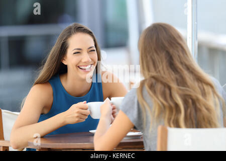 Due amici felice di parlare e ridere seduti in un ristorante con terrazzo Foto Stock