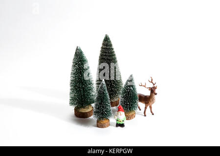 Gruppo isolato di pieno di abeti artificiali come un piccolo albero di foresta in un modello ceramico piastra con una statuetta renna e gnomo da giardino accanto a un bianco Foto Stock