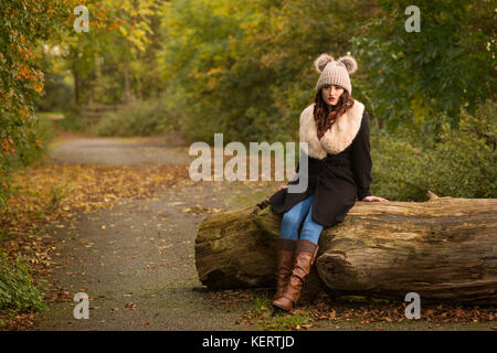 Donna vestita di cappotto e hat seduta sul log in autunno Foto Stock