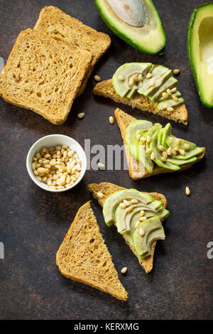 Sandwich di avocado con fresco affettato avocado e pinoli su ardesia scura pietra o sfondo. flat laico, vista dall'alto. Foto Stock