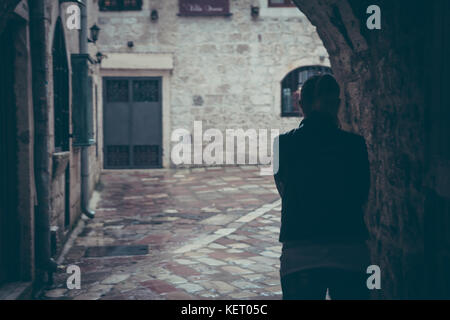 Lonely silhouette di donna a piedi attraverso il buio del tunnel della strada nel giorno di pioggia nella città vecchia durante la pioggia con spazio di copia Foto Stock