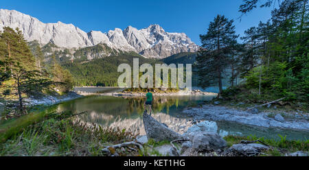 Uomo in piedi sulle rocce, guarda a distanza, lago eibsee lake e il massiccio dello Zugspitze, gamma di Wetterstein, vicino a Grainau, Alta Baviera Foto Stock