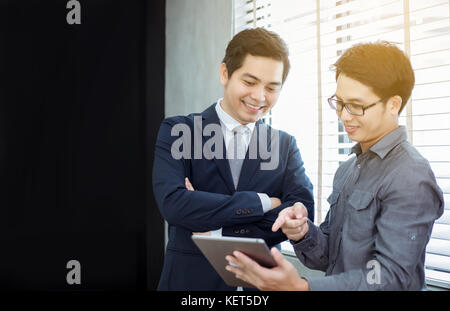 Due asian bello imprenditori utilizzando il touchpad con i partner per discutere i documenti e idee alla riunione e sorridendo felice per il lavoro Foto Stock