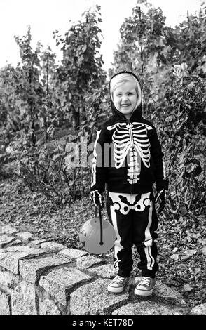 Dolcetto o scherzetto. Bambino contento di indossare il costume di scheletro di halloween all'aperto tenendo la zucca Jack o'Lantern basket Foto Stock