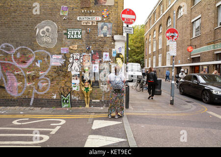 Donna che guarda ad una miriade di arte di strada pezzi sulla parete in corrispondenza della giunzione di Buxton Street e Brick Lane a Londra Inghilterra Foto Stock