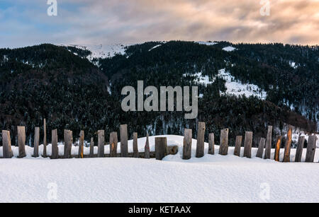 Vecchia staccionata in legno nella neve sulla collina. bellissimo montuoso scenario rurale di sunrise Foto Stock