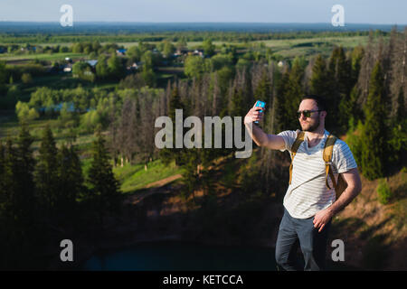 Giovane uomo elegante con la barba indossando occhiali da sole rende selfie sulle pareti del canyon. Foto Stock