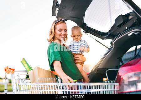 Madre con bambino, mettendo lo shopping nel retro della macchina. Foto Stock