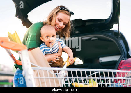 Madre con bambino, mettendo lo shopping nel retro della macchina. Foto Stock