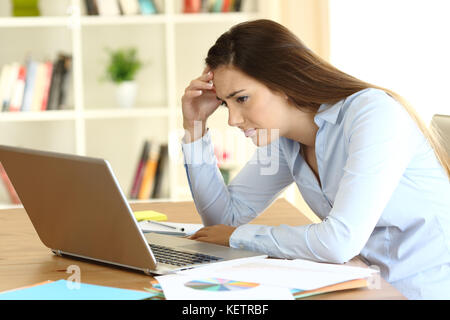 Preoccupato per il lavoratore freelance la lettura di cattive notizie sulla linea in un computer portatile su una scrivania a casa Foto Stock